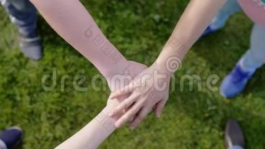 快乐的朋友把手放在草地上，这象征着团结和团队合作